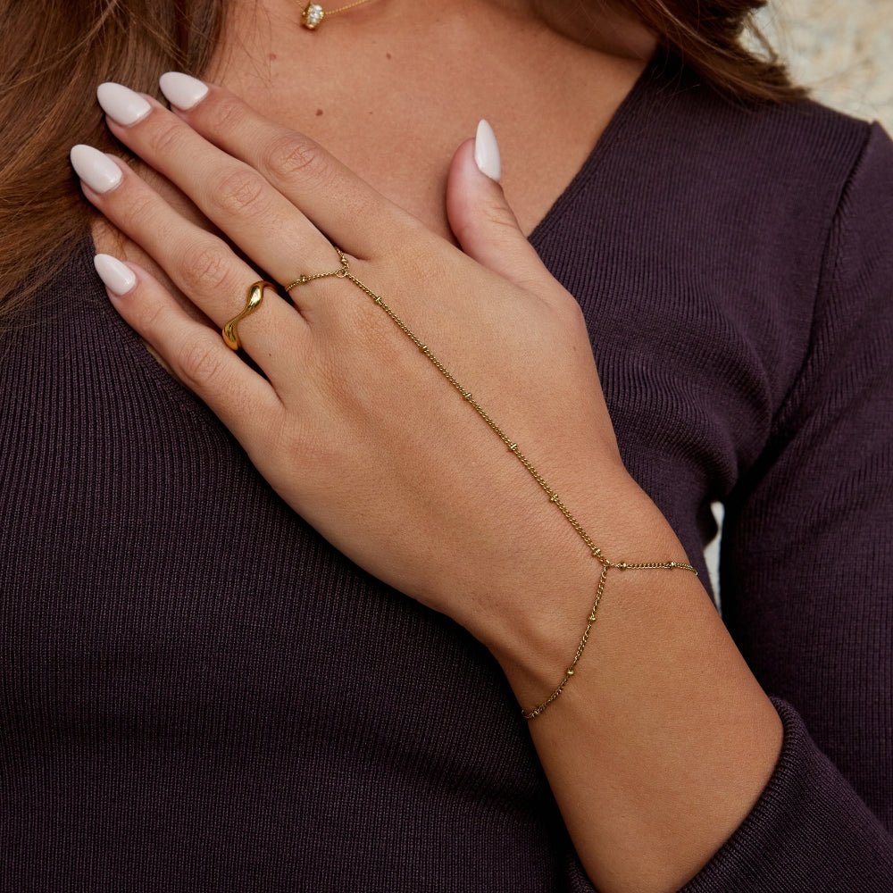 Free 18K Gold Hand Chain Bracelet, worn on a hand with a gold ring and dark top