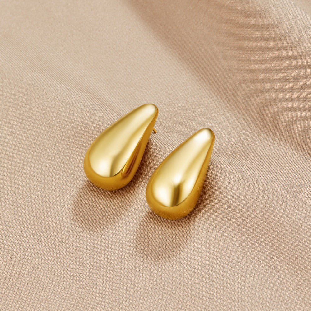 Dakota Gold Teardrop Earrings, pair of polished gold teardrop earrings on beige satin
