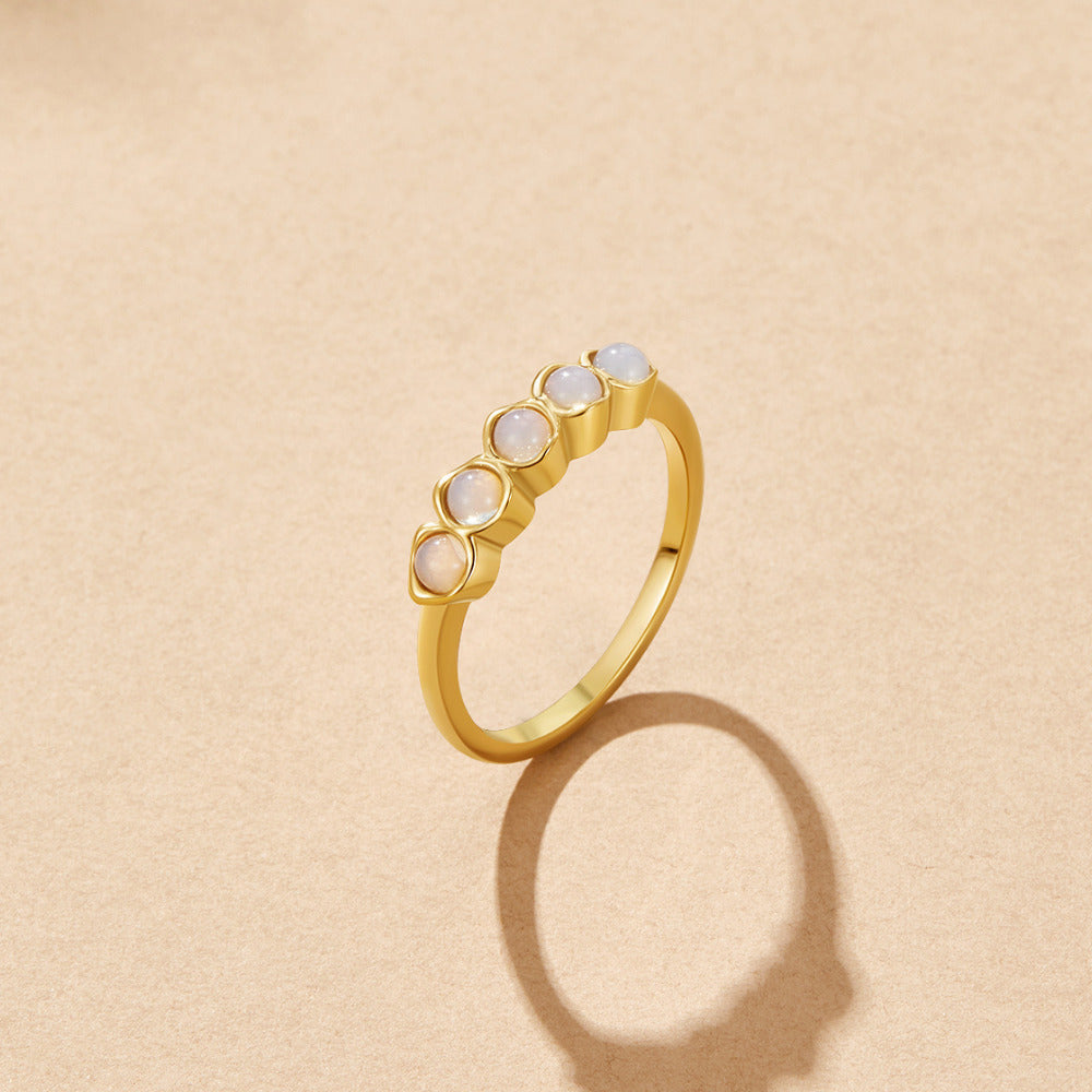 Golden Moonstone Eternity Ring, gold ring with five pale round stones on a beige surface