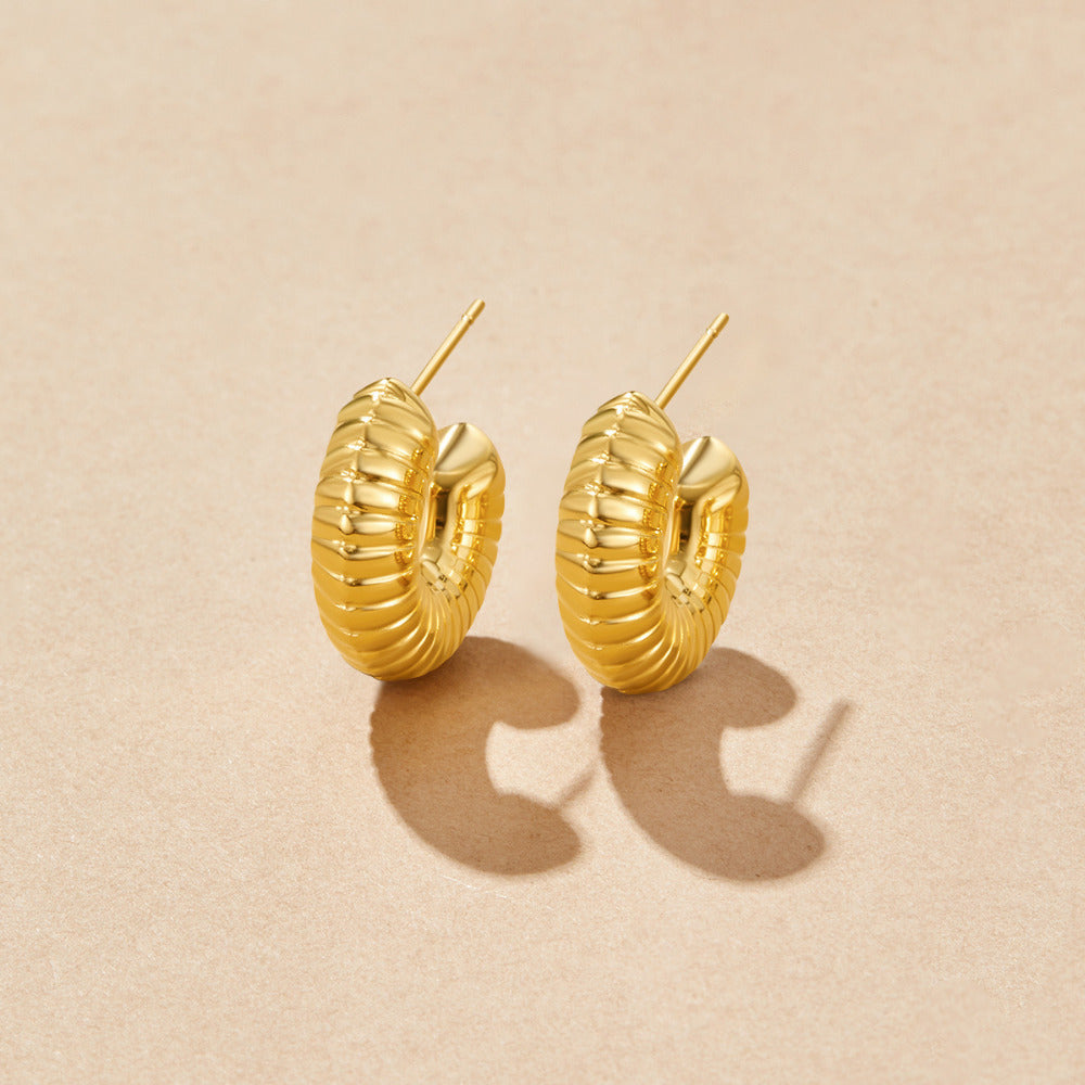 Lulu Spring Hoop Earrings, pair of ridged gold hoops on a beige surface, casting shadows