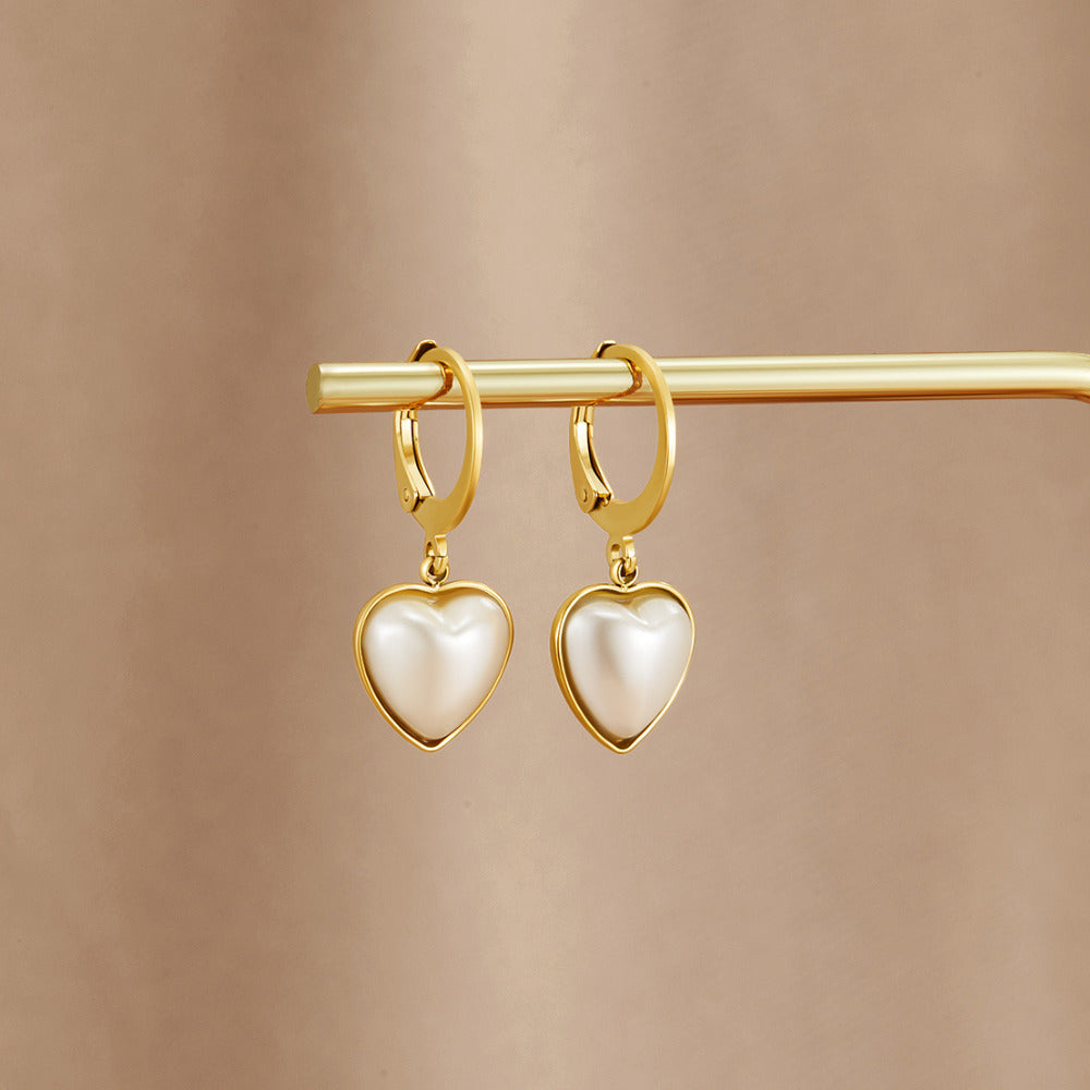 'Pure Heart' Pearl Hoop Earrings, hanging on a gold bar against a beige backdrop, pearl hearts in gold settings