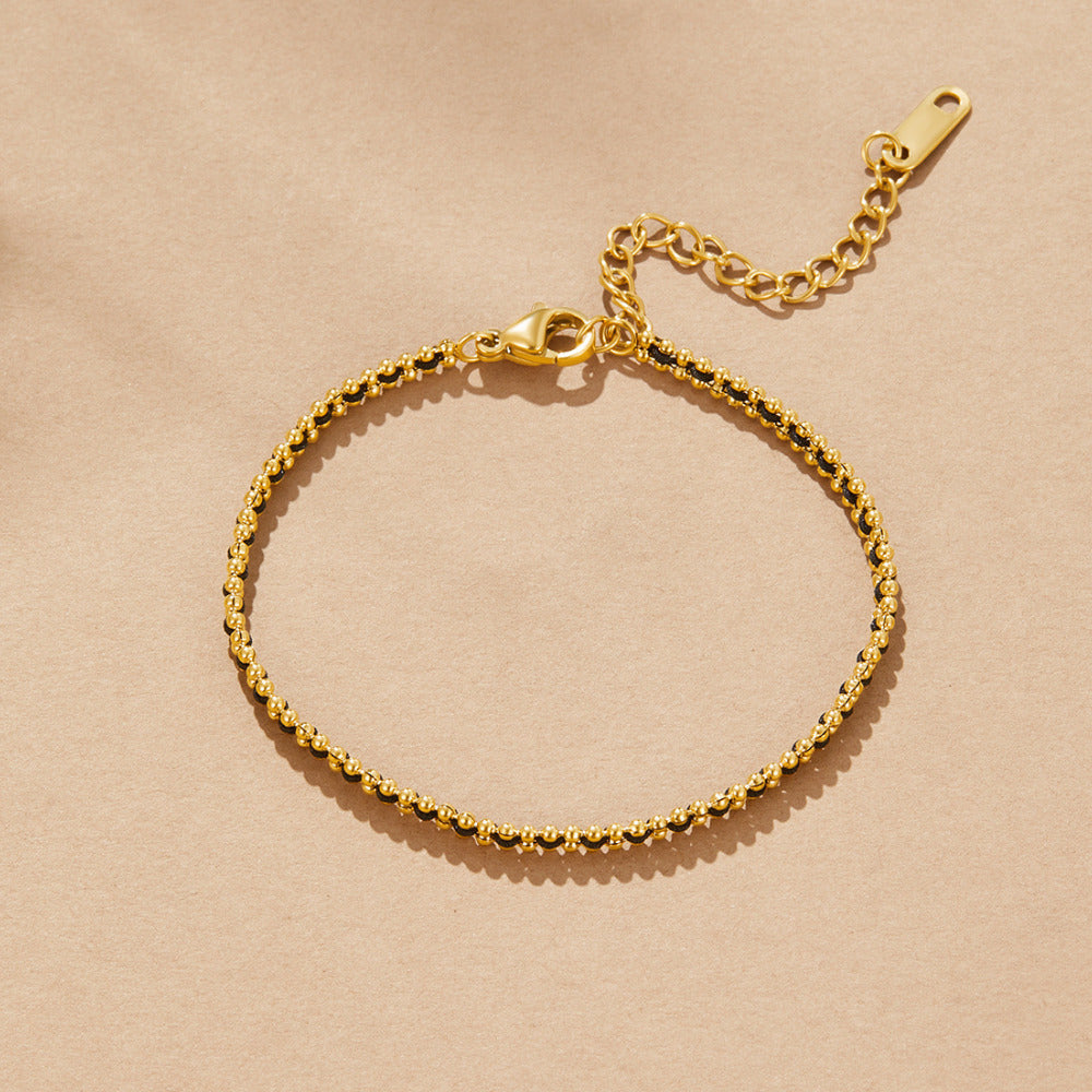 Sofia Bead Chain Bracelet, laid flat on a beige surface, gold beaded chain with black accents