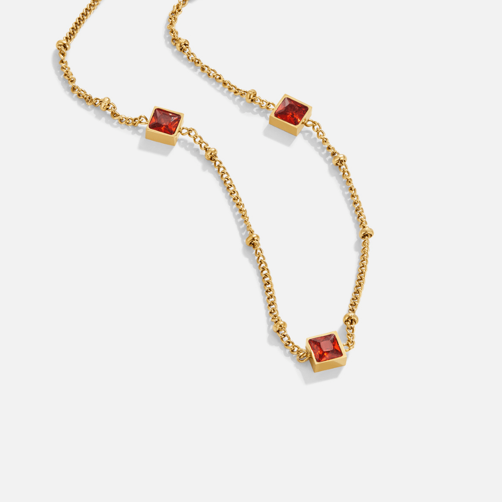Alberta Red Crystal Necklace, laid flat on white, three square red stones on gold chain