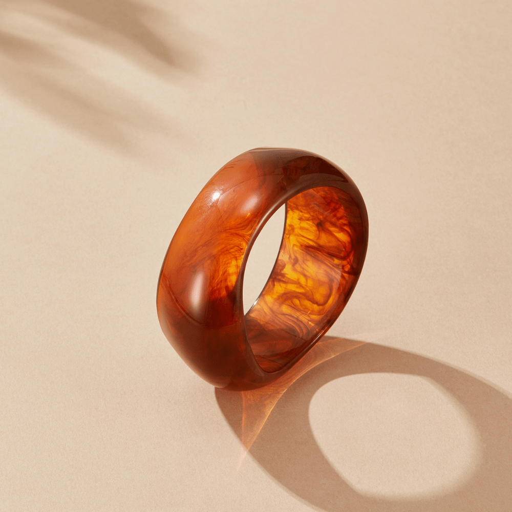 Amber Swirl Bangle, standing on its edge on a beige surface, amber swirled resin