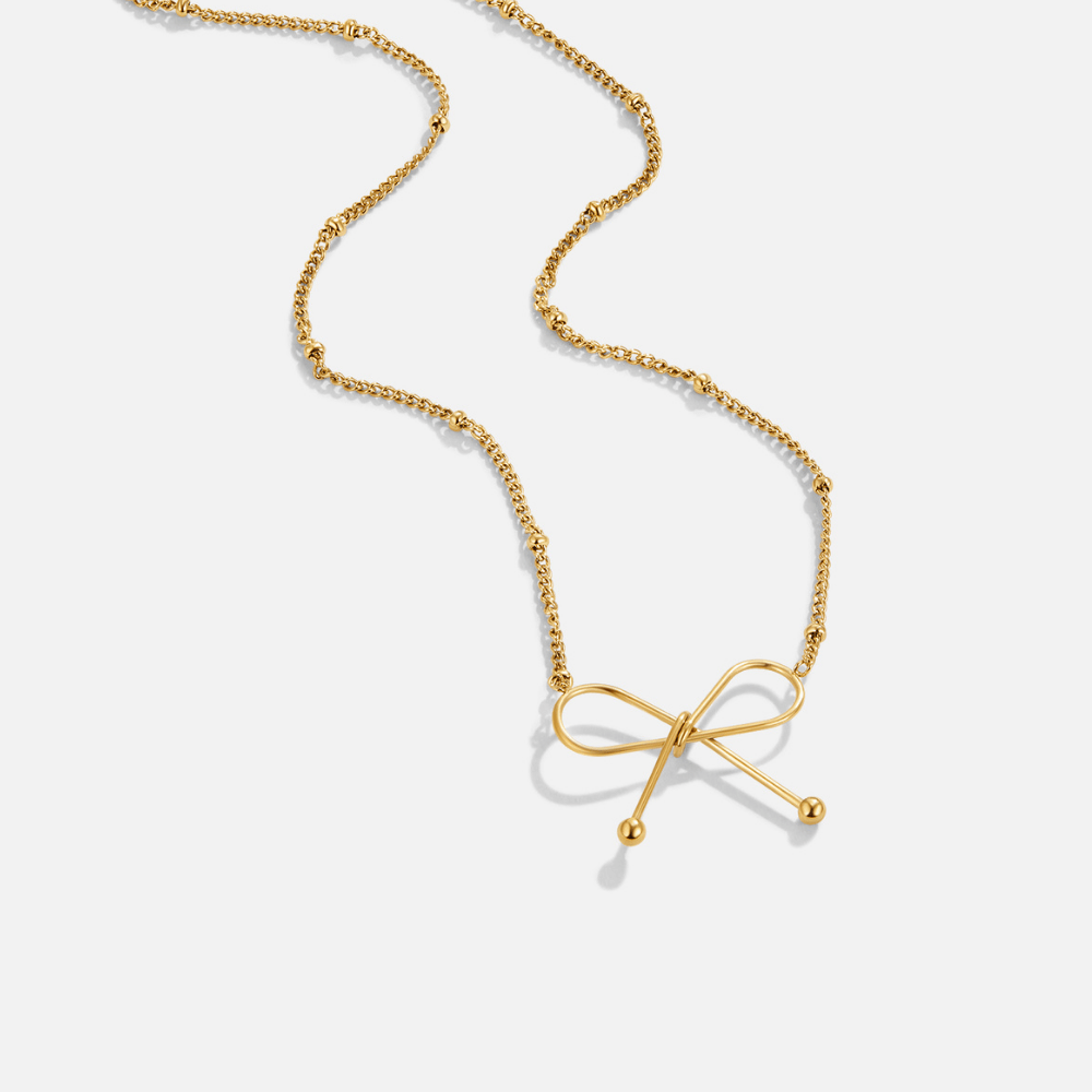 Anika Gold Bow Necklace, gold necklace lying flat on a pale grey background