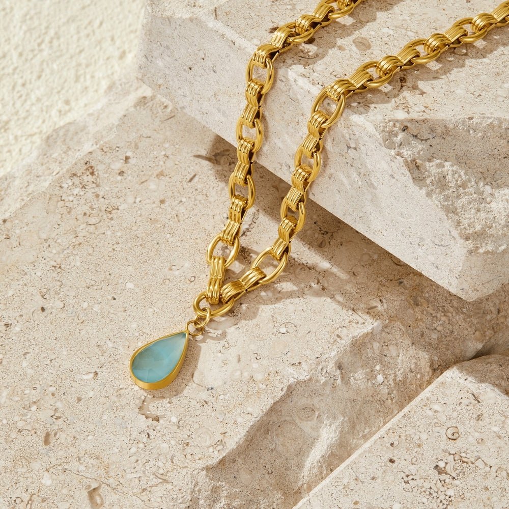 Aqua Stone Drop Gold Chain Necklace, laid across pale stone with a turquoise teardrop pendant