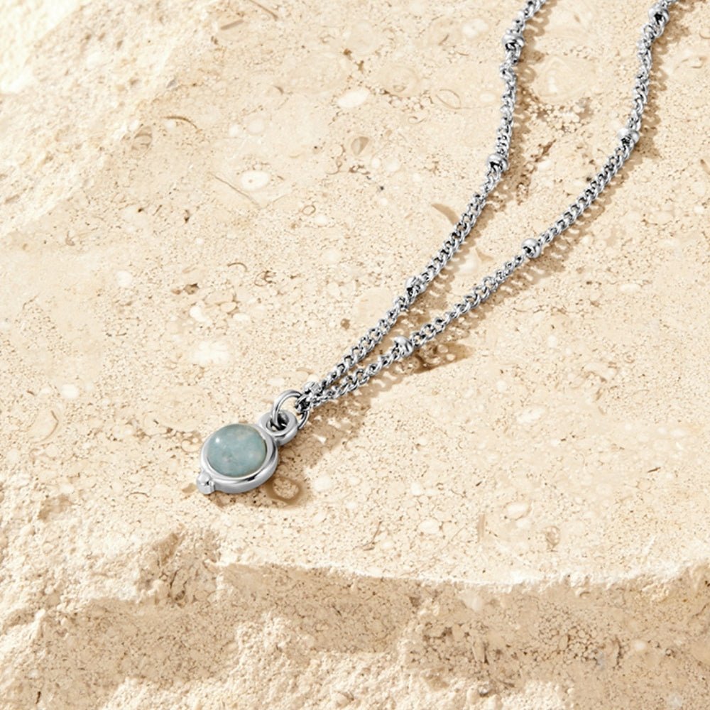 Aquamarine Silver Necklace, laid flat on sandstone, with a pale blue round pendant in silver