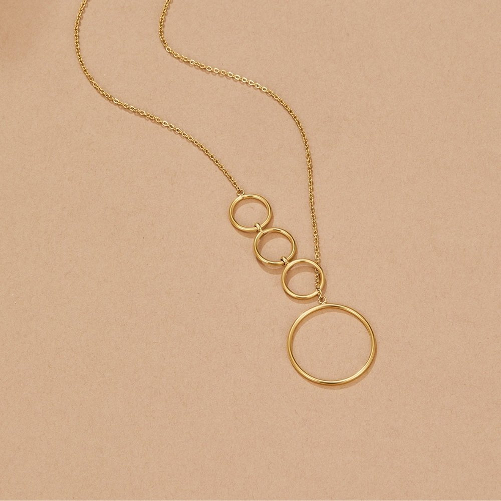 Aspen Gold Long Necklace, laid flat on a beige surface, gold chain with graduated rings