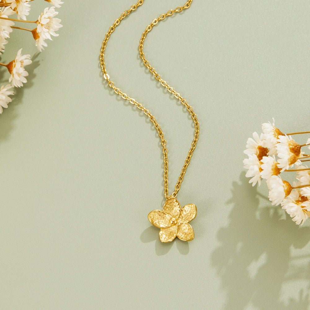 Blooming Gold Flower Necklace, laid flat on sage green with dried white flowers around it