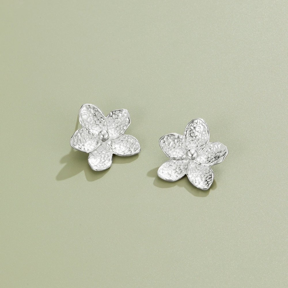 Blooming Silver Flower Earrings, pair of hammered silver flower earrings lying on sage green