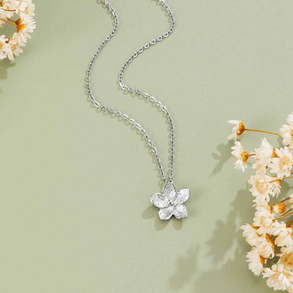 Blooming Silver Flower Necklace, flat lay on sage green with dried white flowers at the edges