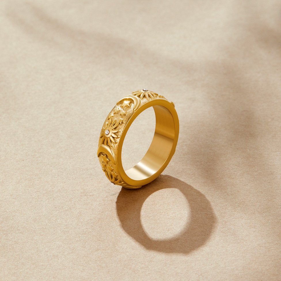 Celestial Gold Ring, standing upright on beige paper, gold band with sun and moon relief