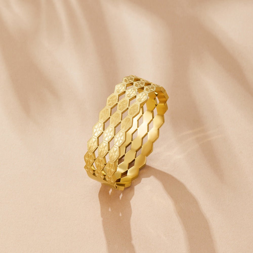 Celine Geometric Gold Bangle, standing on edge on a peach surface, geometric gold openwork