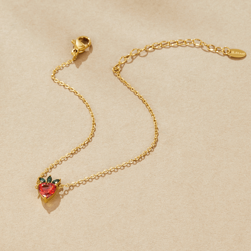 Crystal Berry Bracelet, laid flat on beige fabric, gold chain with red strawberry charm