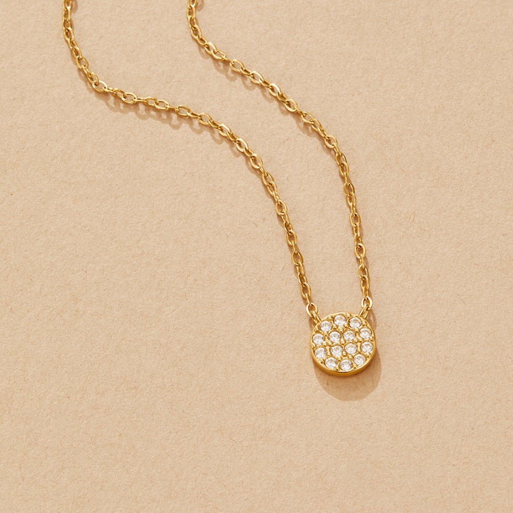 Elaine Crystal Disc Necklace, laid flat on a beige surface, gold chain with pavΓ© disc pendant