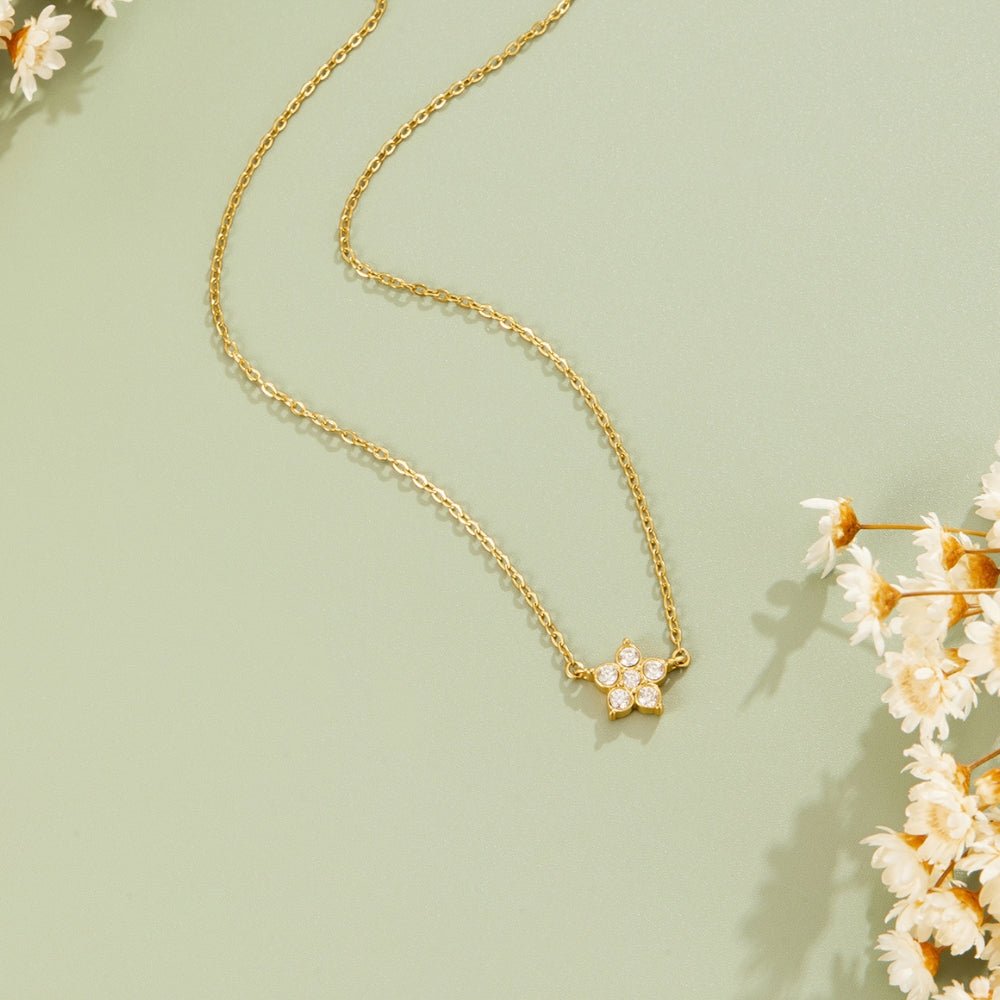 Elara Crystal Bloom Gold Necklace, laid flat on sage green with dried white flowers beside it