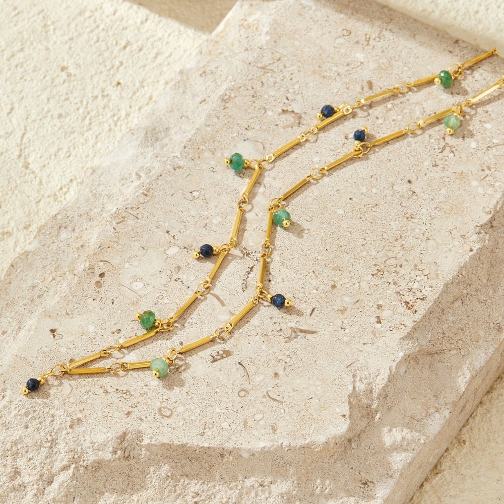 Elara Stone Droplet Necklace, two gold bar-link chains with green and blue beads, laid on pale stone