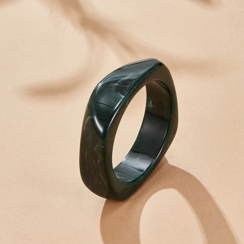 Emerald Swirl Bangle, dark green marbled bangle lying flat on a beige surface