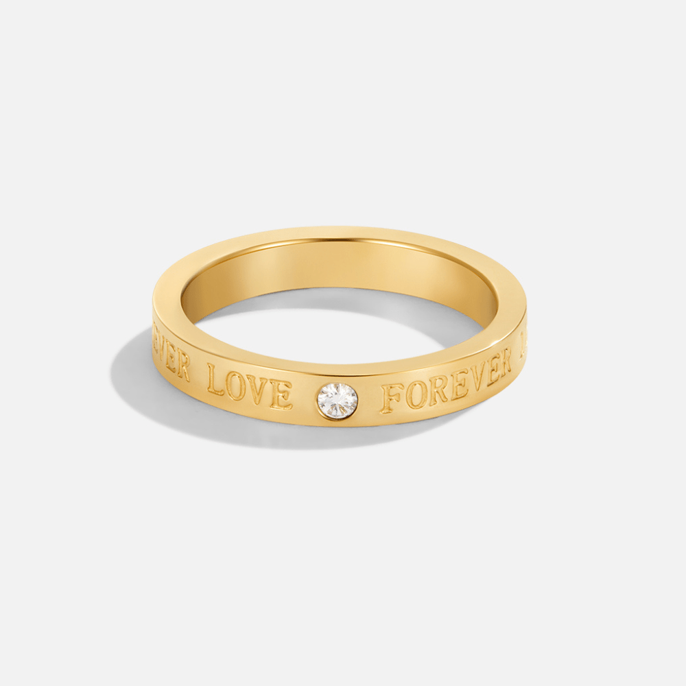 Forever Love Crystal Gold Ring, standing upright on plain grey, gold band with a single clear stone