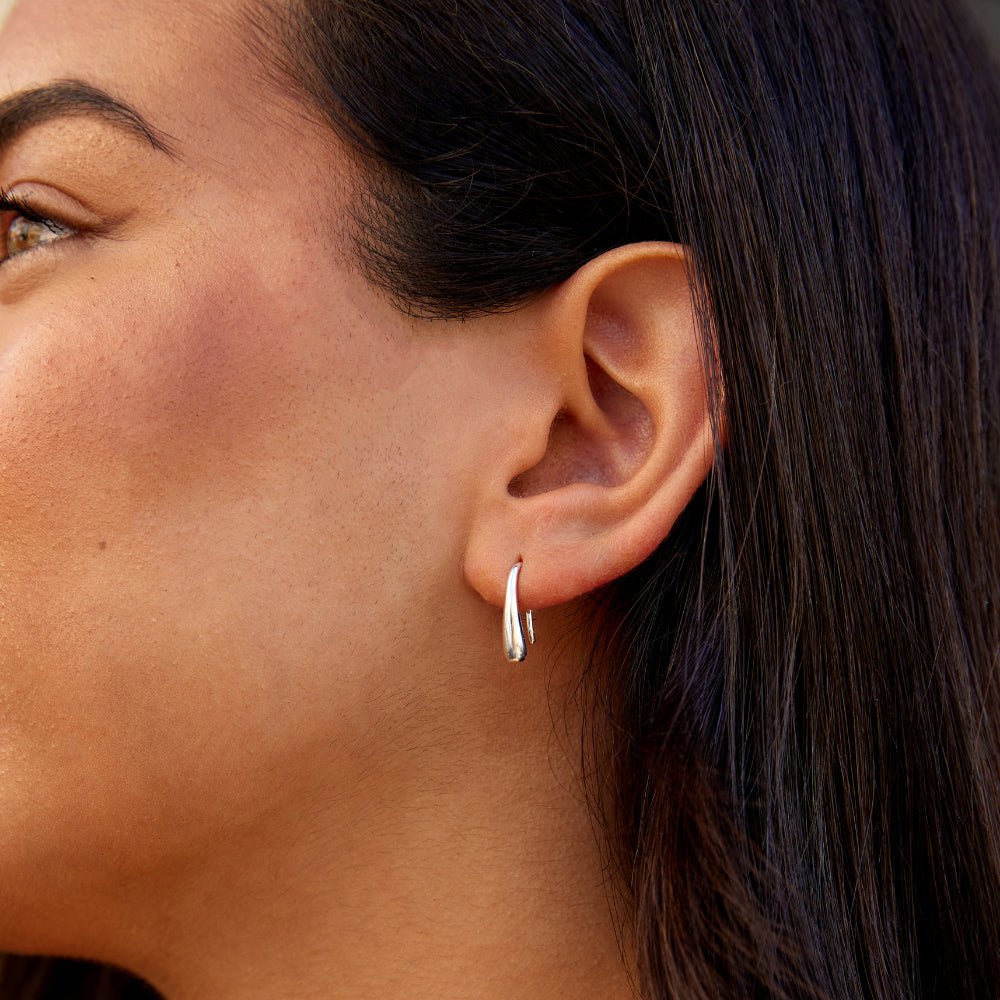 Francesca Water Drop Silver Earrings, worn on an ear, close-up of a smooth silver teardrop hoop