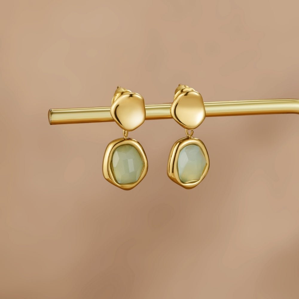 Gold Aquamarine Drop Earrings, hanging on a gold rod, pale green stones, against beige