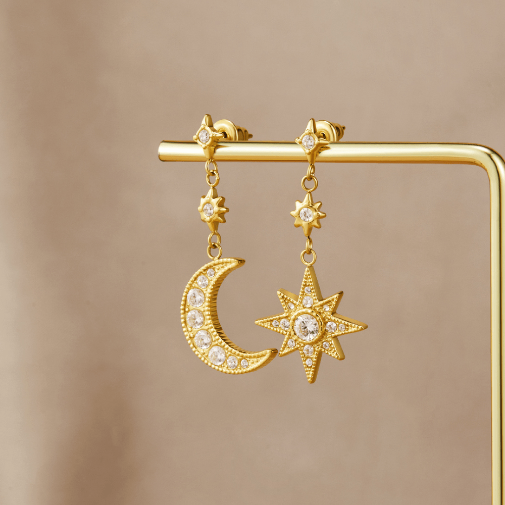Gold Crystal Moon & Star Earrings, hanging on a gold display stand against a beige backdrop