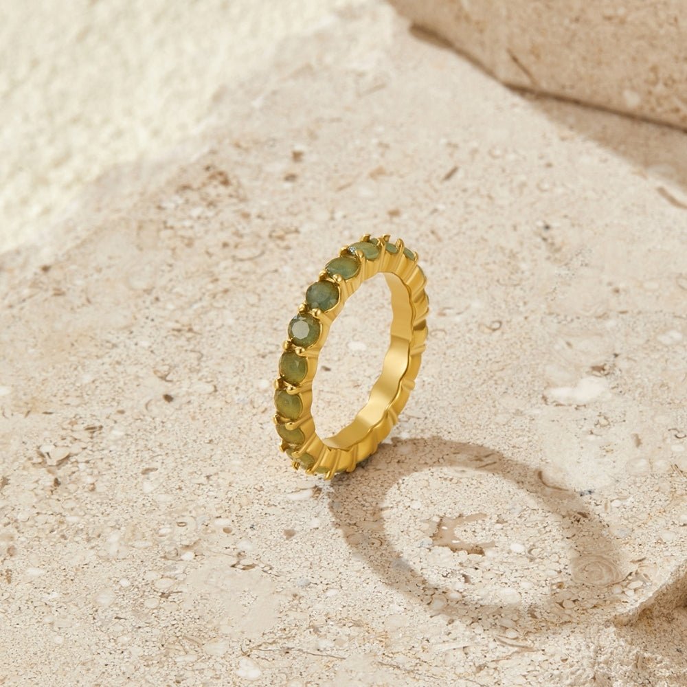 Gold Eternity Moonstone Ring, standing upright on sandy stone with green gemstones and gold