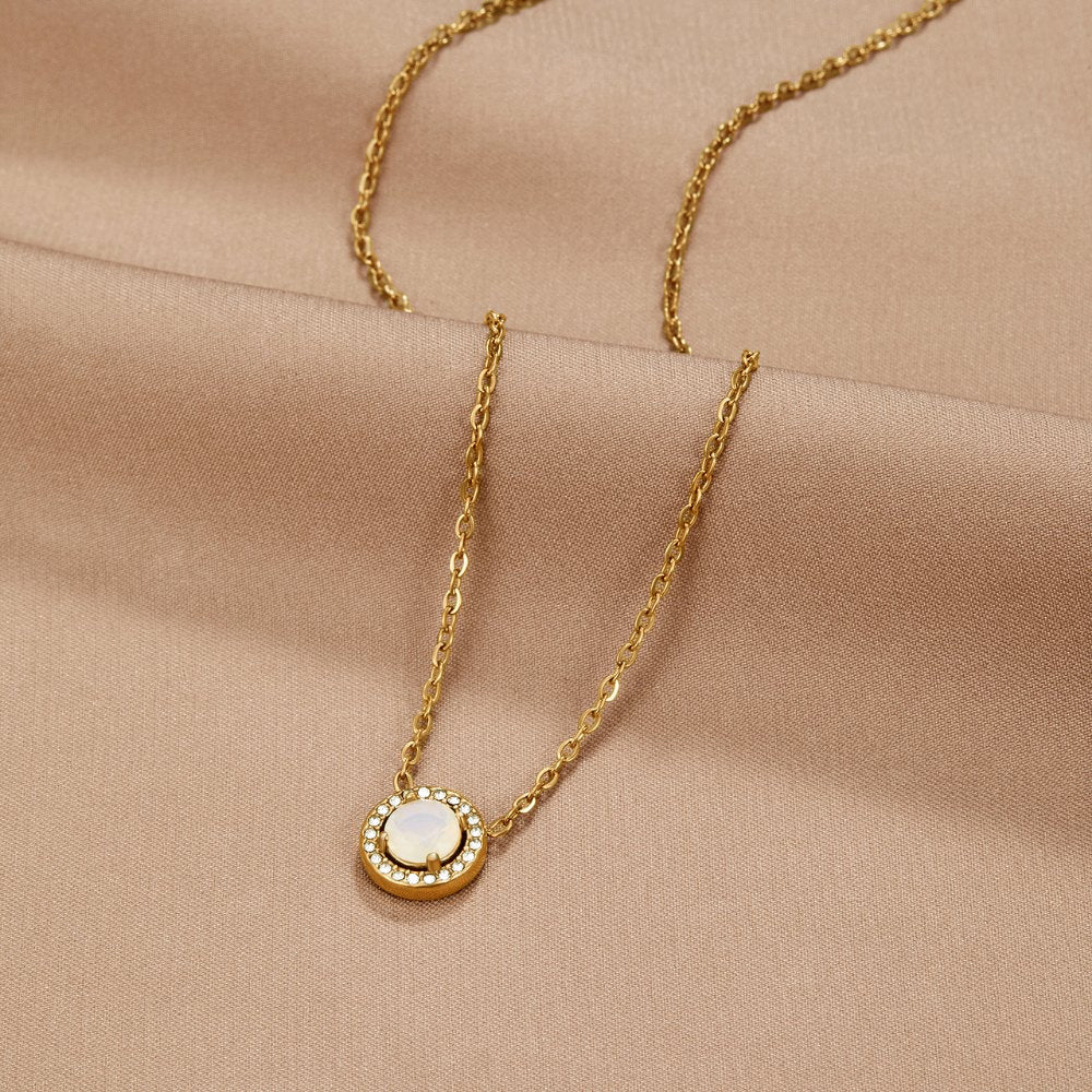 Gold Monet Crystal Necklace, laid flat on beige satin, round white stone with crystal halo