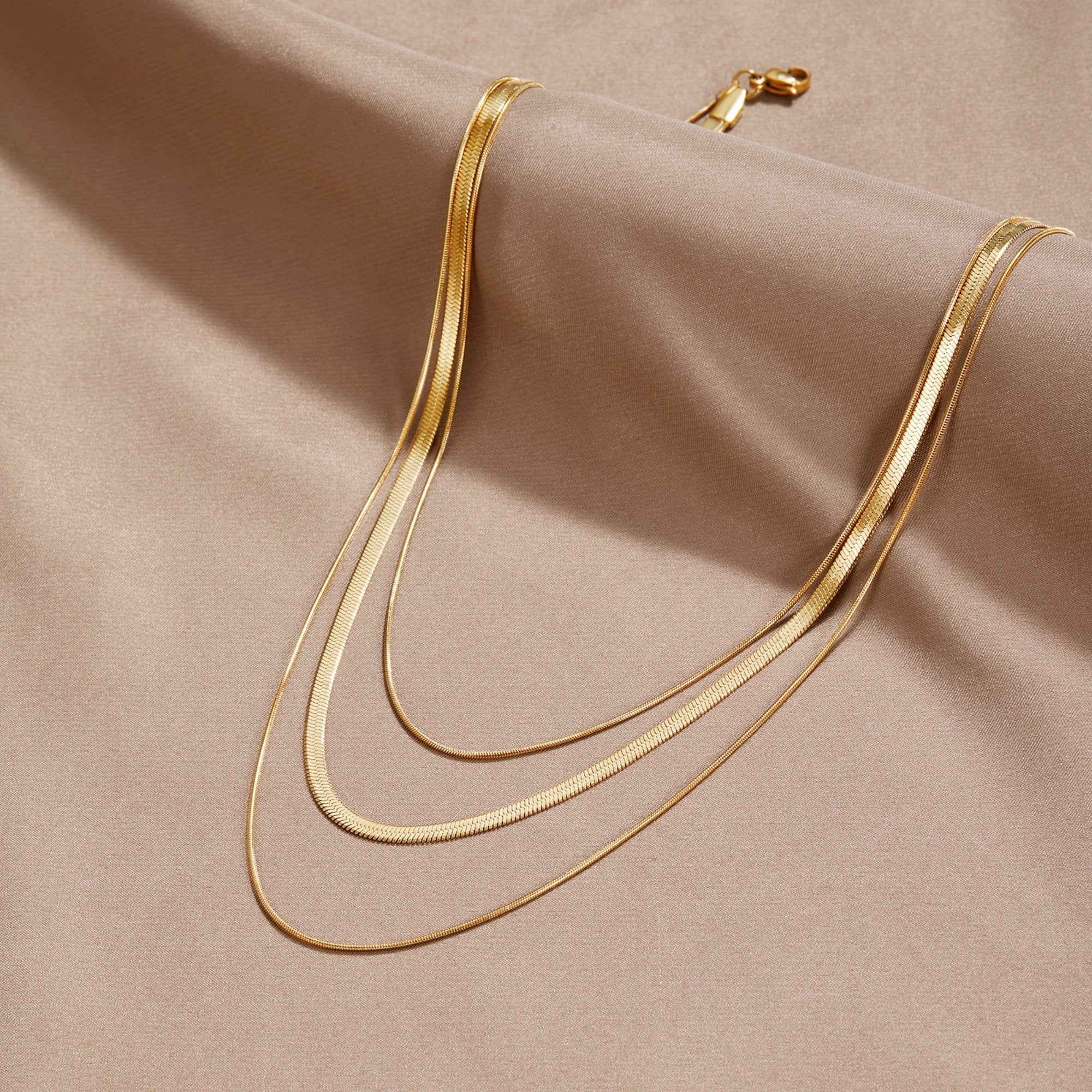 Gold Multi-Layered Chain Necklace, three gold chains layered on beige fabric, lobster clasp at