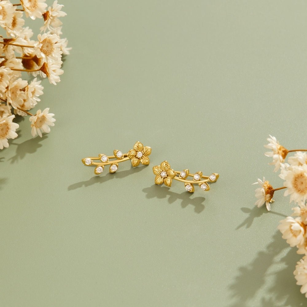 Golden Crystal Vine Earrings, pair of gold vine earrings on sage green, beside dried white flowers