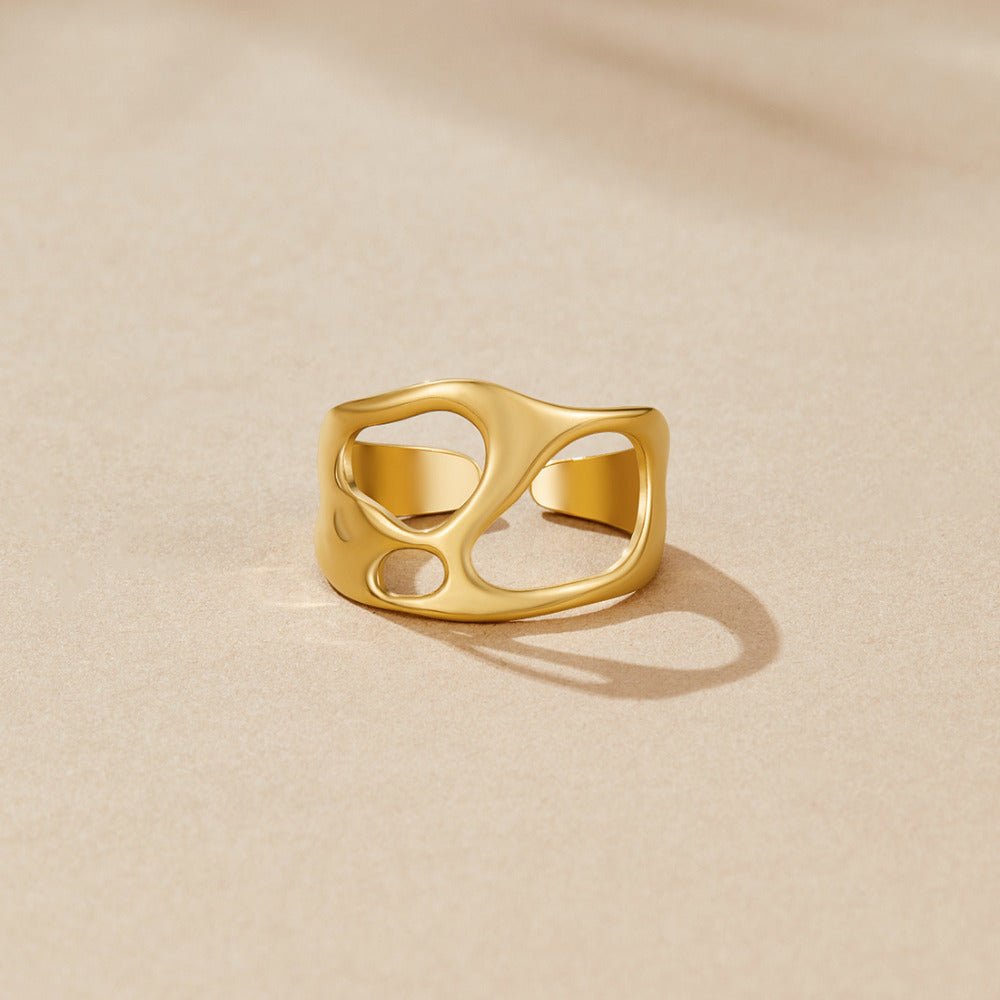 Golden Dream Hollow Ring, wide gold ring with cut-out openings, lying on a beige surface