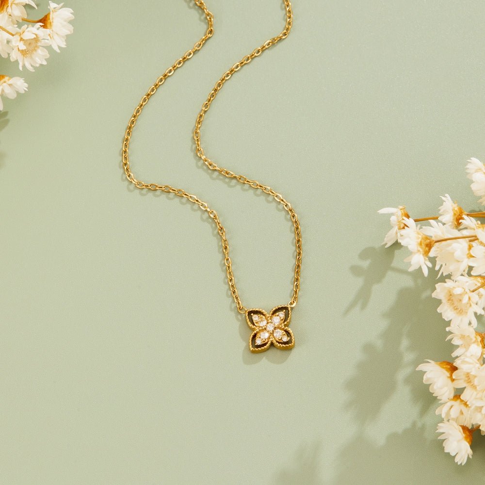 Golden Four Leaf Crystal Necklace, laid flat on sage green with dried white flowers, pendant
