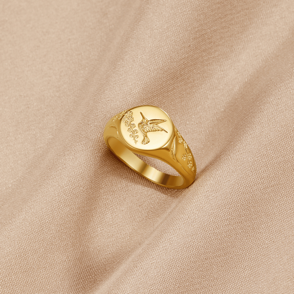 Golden Hummingbird Signet Ring, gold signet ring on beige fabric, engraved hummingbird on face