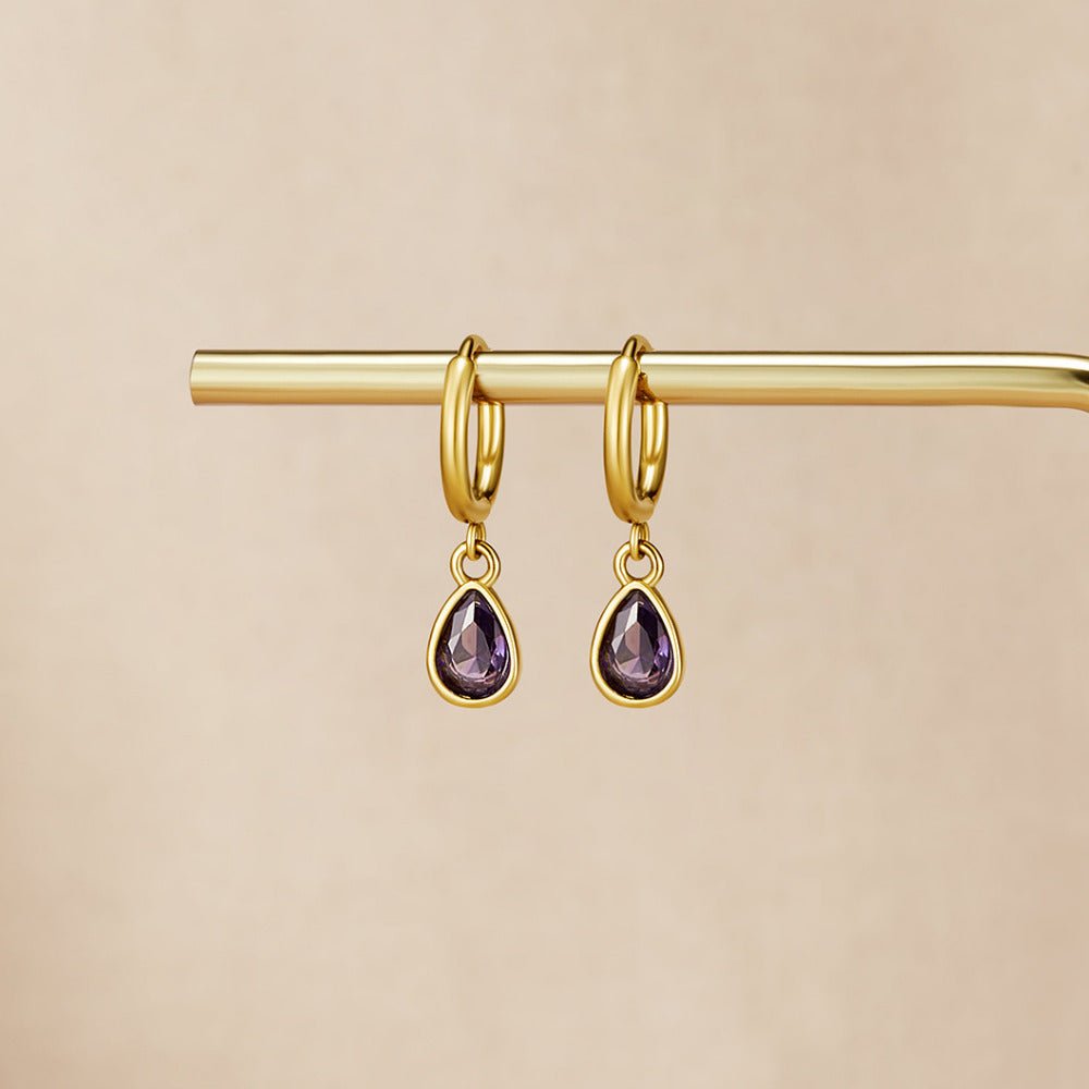 Golden Purple Teardrop Earrings, hanging from a gold bar on a beige backdrop, purple teardrop stones