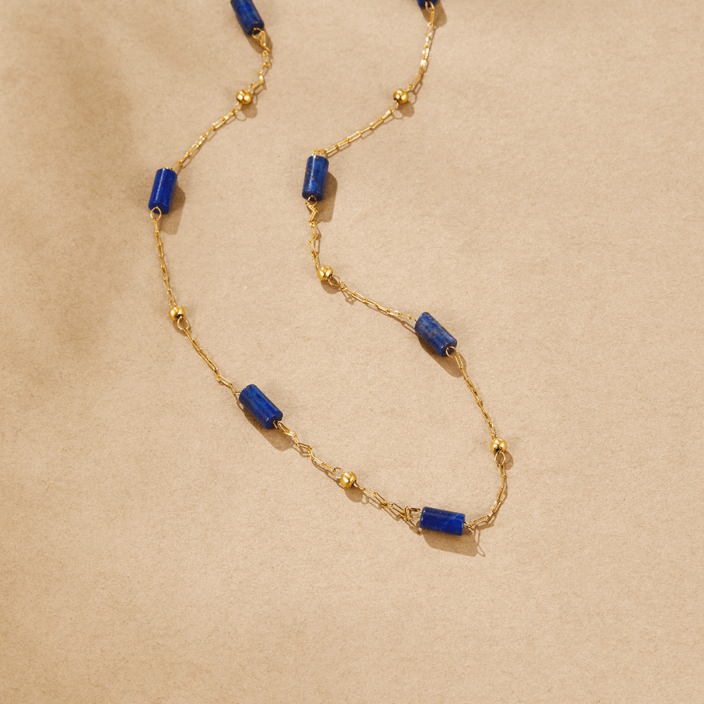 Lapiz Lazuli Bead Necklace, laid flat on sand-coloured paper, gold chain with blue cylinder beads