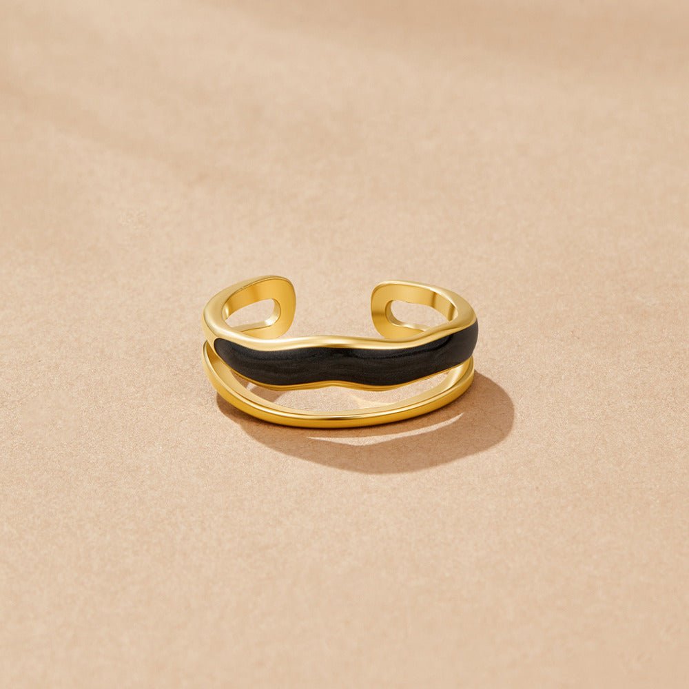 Layered Black Sahara Gold Ring, gold open band with wavy black enamel stripe, on beige surface