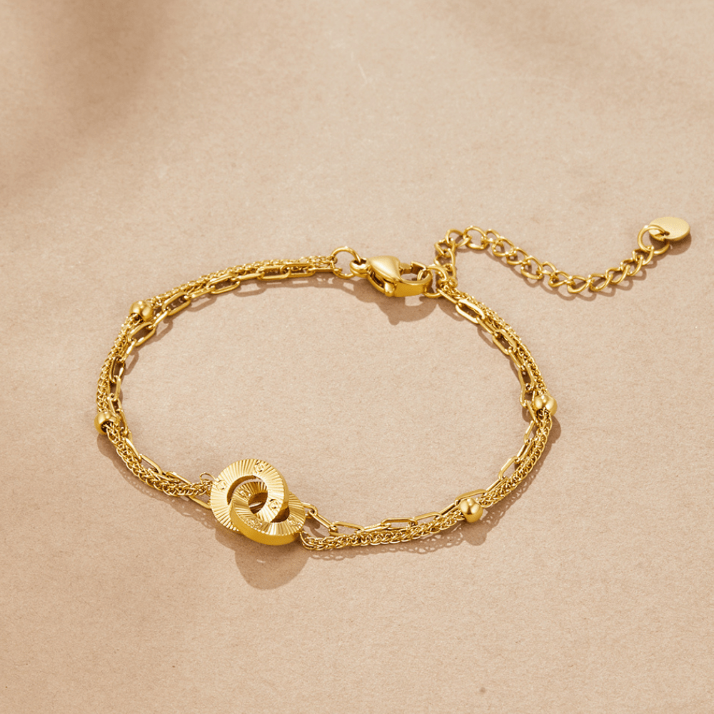Layered Eternity Loop Bracelet, laid flat on beige paper, double gold chain with interlocking