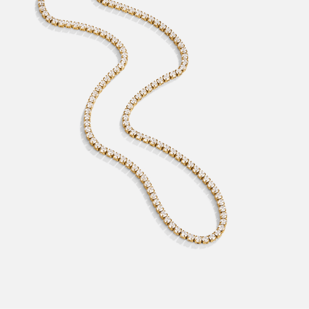 Cordelia Gold Crystal Necklace, gold tennis necklace laid out in a winding curve on white