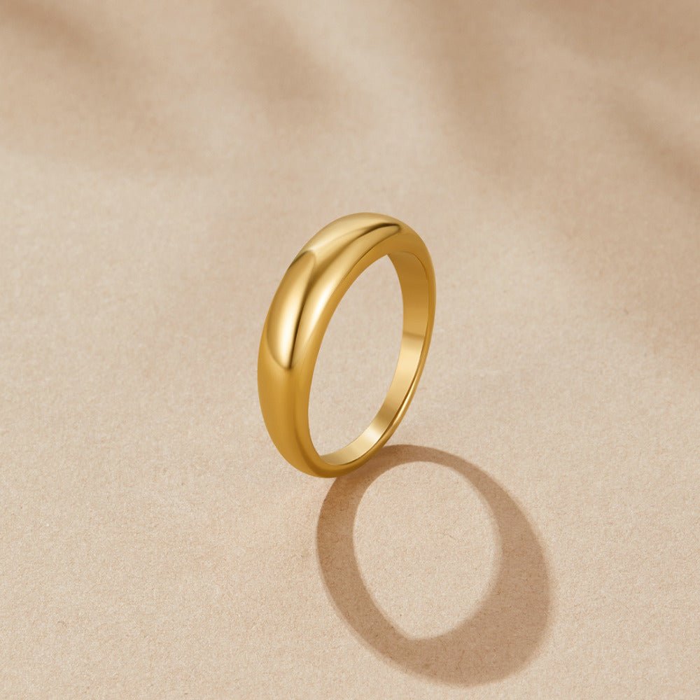 Lois Gold Band Ring, standing upright on beige paper, polished gold dome band