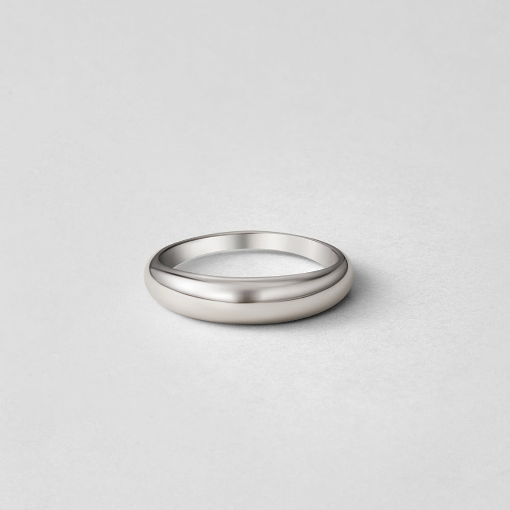 Lois Silver Band Ring, standing on its edge on a pale grey surface, polished silver