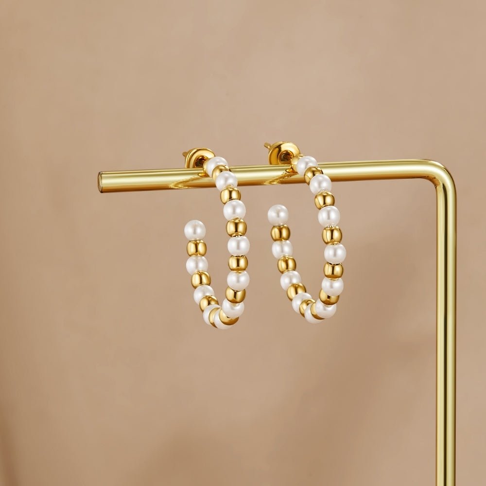Maia Pearl & Gold Bead Earrings, hanging on a gold display stand against a beige backdrop