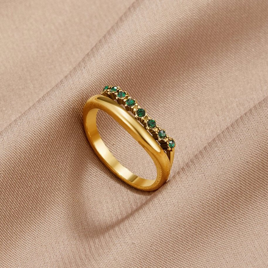 Marissa Emerald Green Layered Ring, gold ring with a row of green stones, resting on beige satin