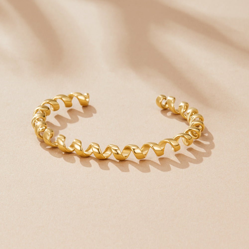 Melinda Gold Coil Bracelet, open gold cuff with twisted coil pattern on beige surface