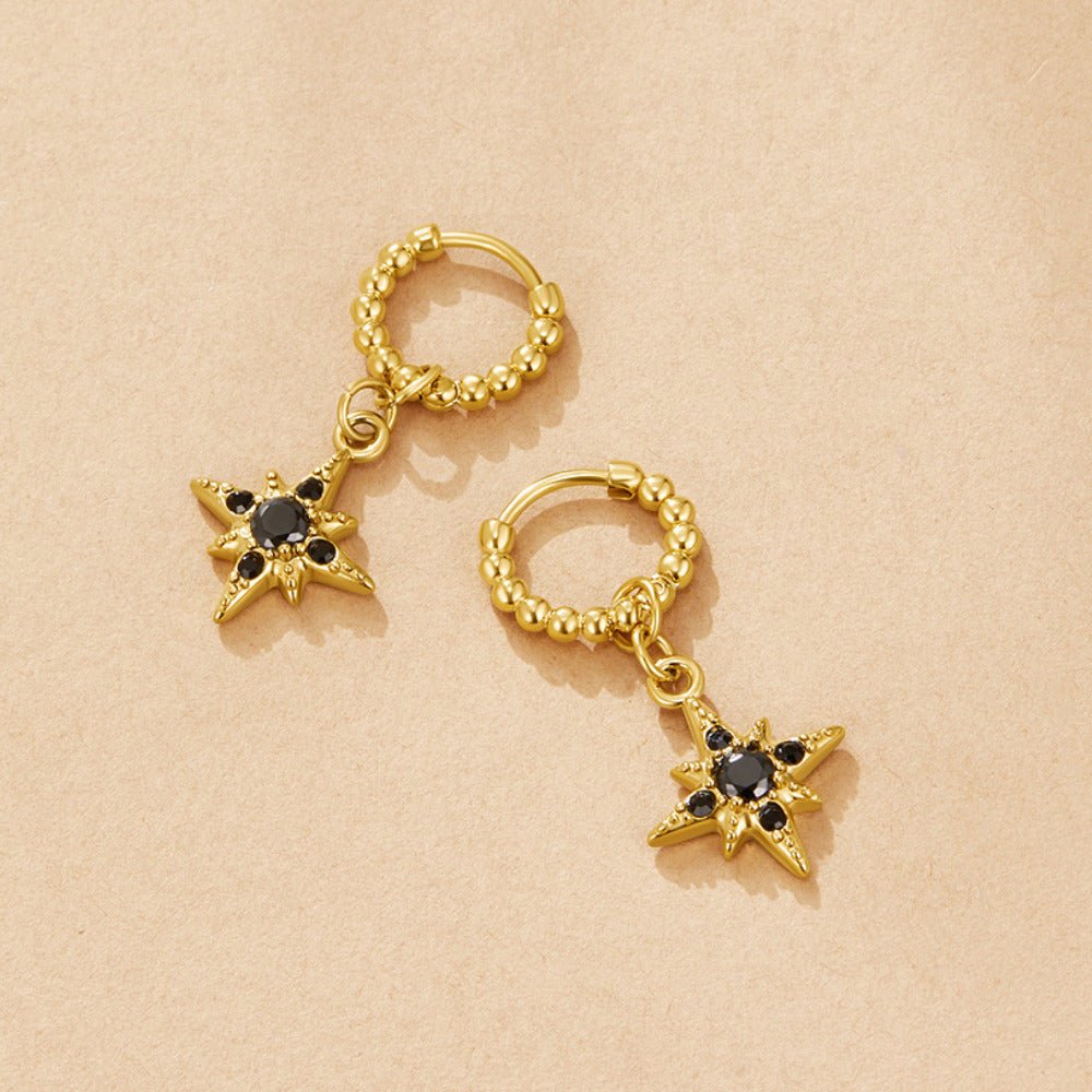 Midnight Luxe Drop Hoop Earrings, pair of gold hoops with star charms on beige surface