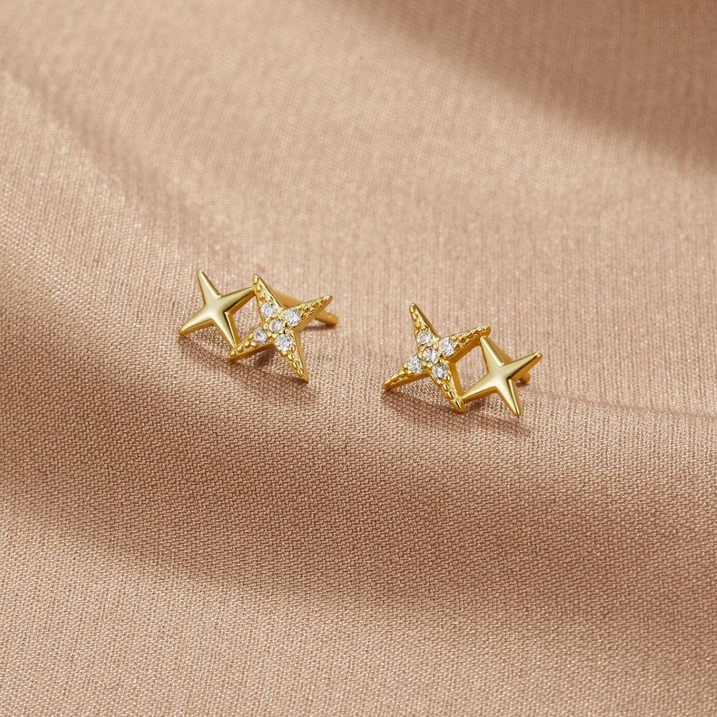 Midnight Magic Studs, pair of gold star studs on a beige fabric, one with small clear stones