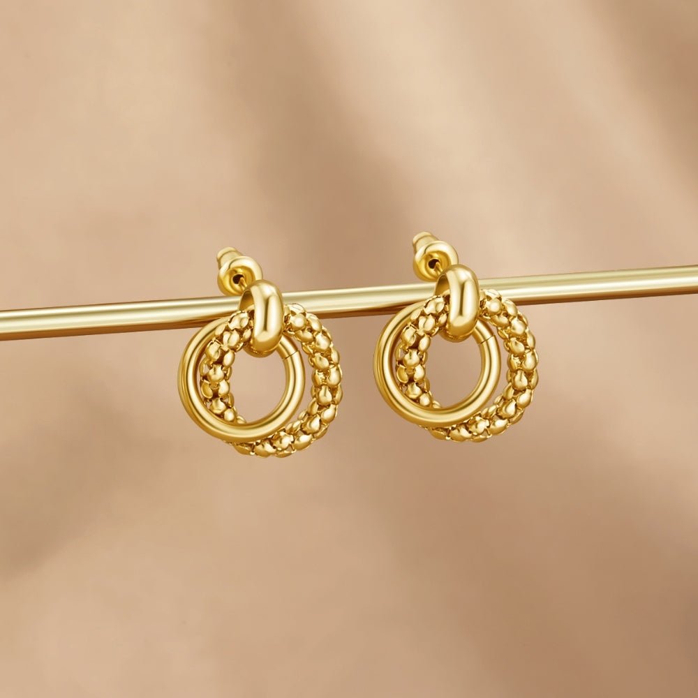 Monica Twisted Bead Hoop Earrings, a pair of gold earrings hanging from a gold rod against a