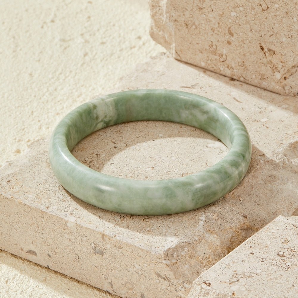 Natural Jade Stone Bangle, lying flat on stone blocks, pale green marbled surface