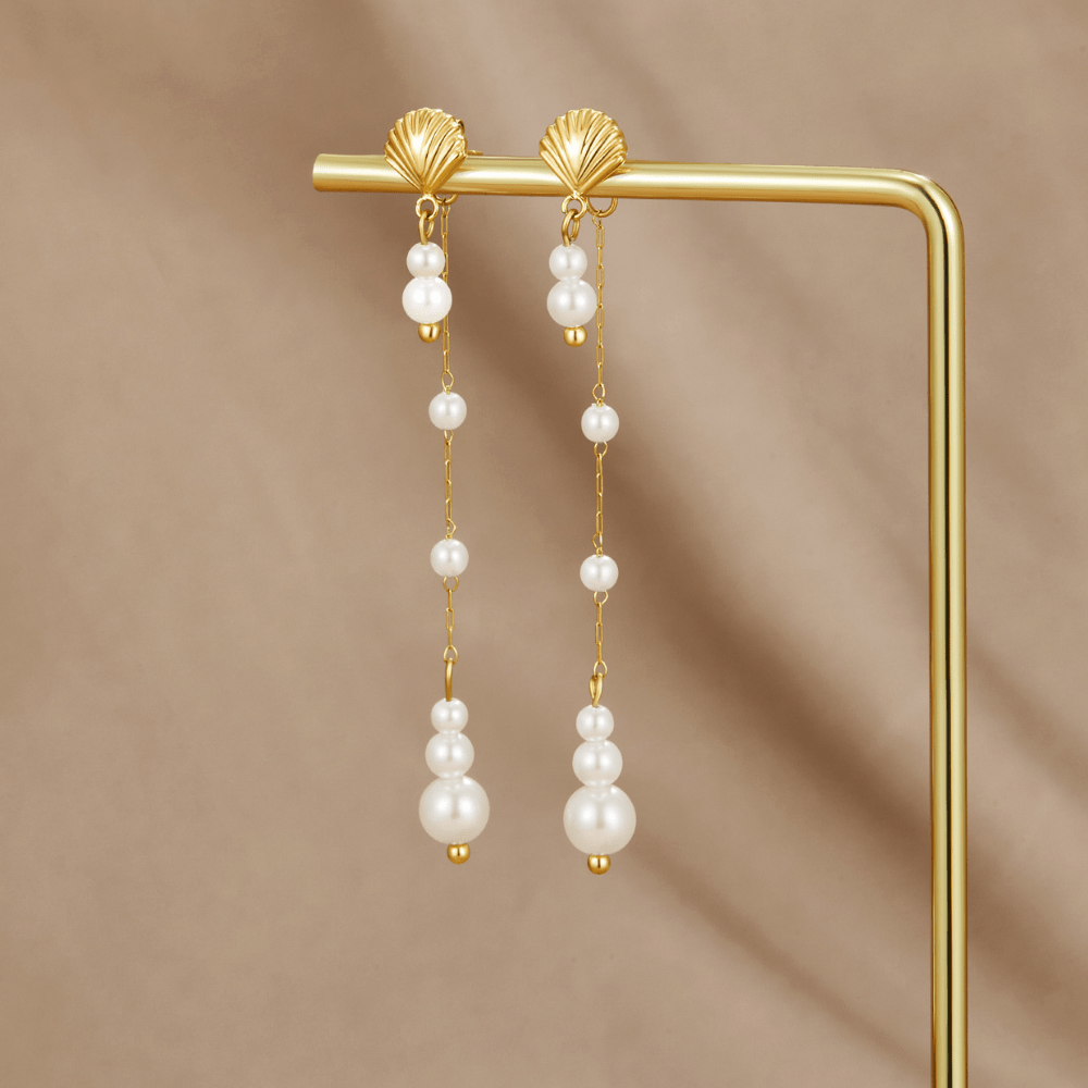 Neesa Pearl Tassel Earrings, pair of gold shell earrings with graduated pearl drops, hung on a gold display stand