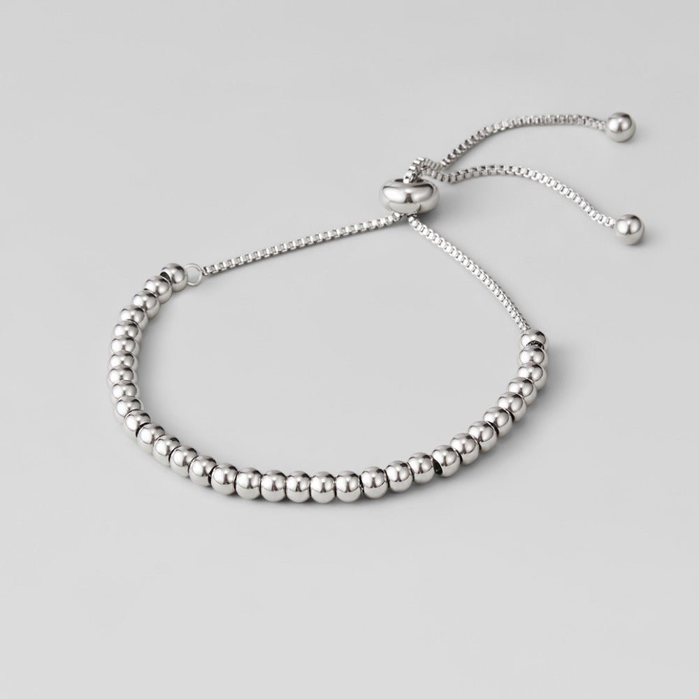 Niloya Beaded Silver Bracelet, laid flat on a grey surface, silver beads with a sliding clasp