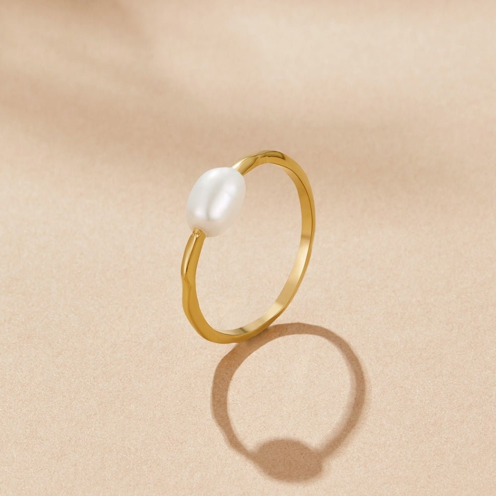 Nura Freshwater Pearl Ring, standing upright on beige surface, gold band with oval white pearl